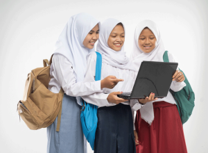 three-girls-veils-school-uniforms-stand-smiling-using-laptop-together-while-carrying-backpacks